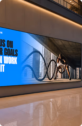Athlete exercising with battle ropes in an urban indoor gym under a large screen with motivational text.