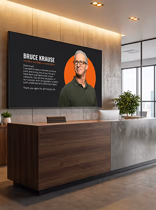 Modern office lobby with wood and concrete reception desk and screen showing Bruce Krause's message.