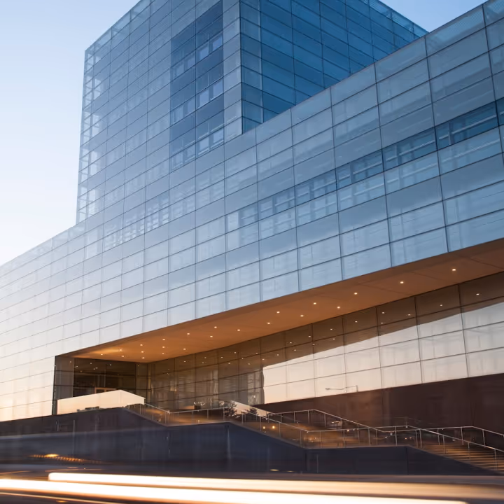 Modern glass building with illuminated entryway and light trails from passing cars.