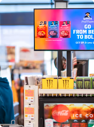 Store counter with energy drinks and a screen showing Quaker Fruit Fusion cereal advertisements.
